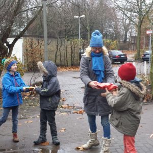 Schüler der Schule Rothestrasse überreichen Geschenke und stehen warm eingepackt draußen auf einem Anwohnerparkplatz.